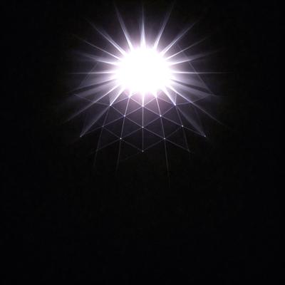 The primary subject of the image is a bright light source, possibly a star or a light bulb, shining in a dark environment. The light source is surrounded by a pattern of lines, which adds an interesting visual element to the scene. The setting appears to be a black background, which further emphasizes the brightness of the light source. The visual style of the image is a combination of a photo and a pattern, creating a unique and captivating image. The colors and mood of the image are predominantly dark, with